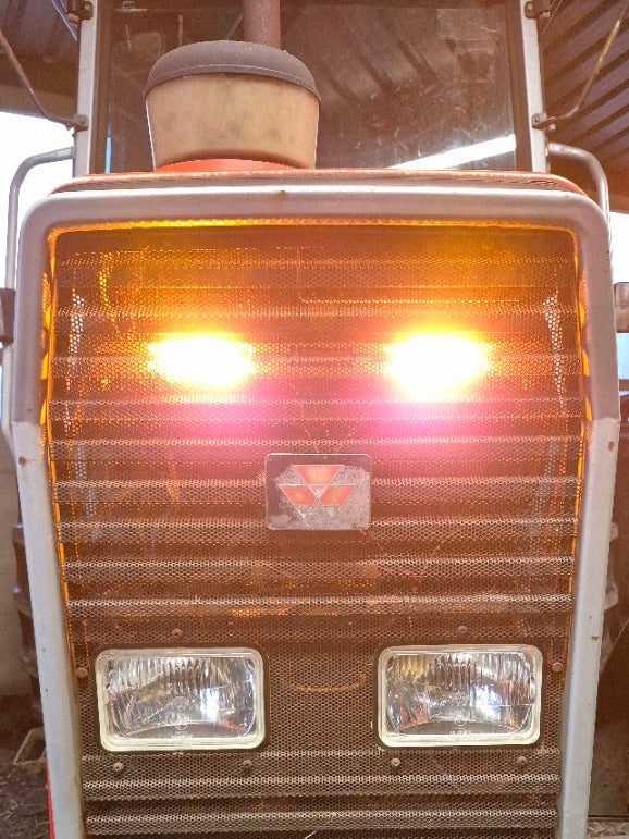 Close-up of the front end of a Massey Ferguson tractor with the flash tractor kit lights on, showing the powerful front grille and distinctive Massey Ferguson logo.